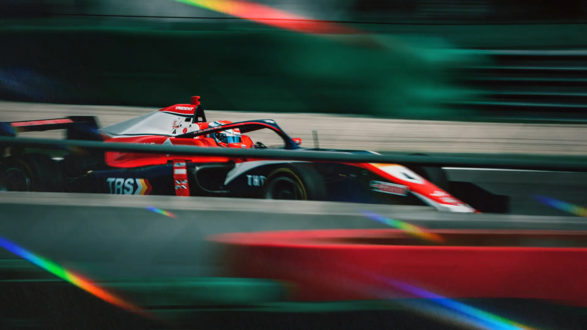 A single-seater Formula racing car in red, white and navy sponsor livery speeding along a track in motion blur, illustrating a guide to F1 sponsors and official partners in 2026.