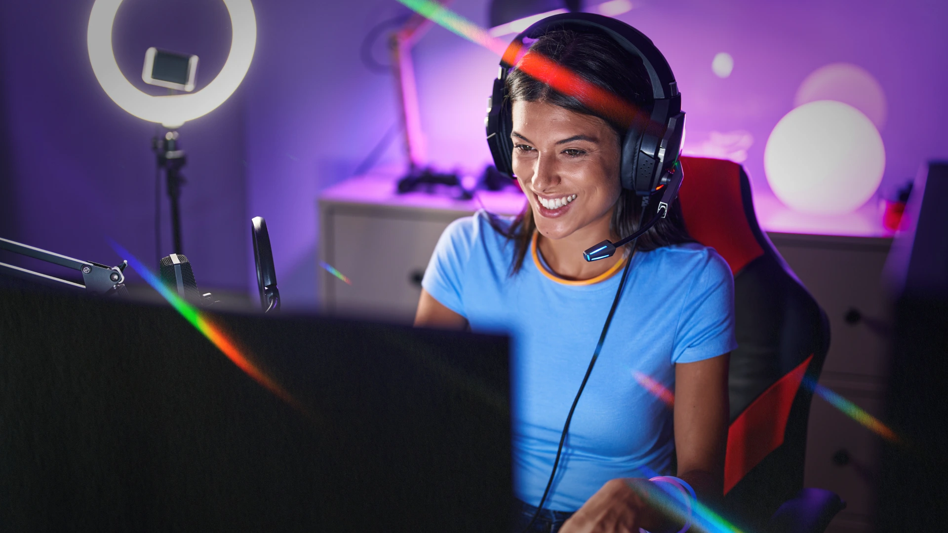 A smiling content creator streaming from a home gaming setup with headset, microphone and ring light, representing the influencer campaigns brands measure ROI on.