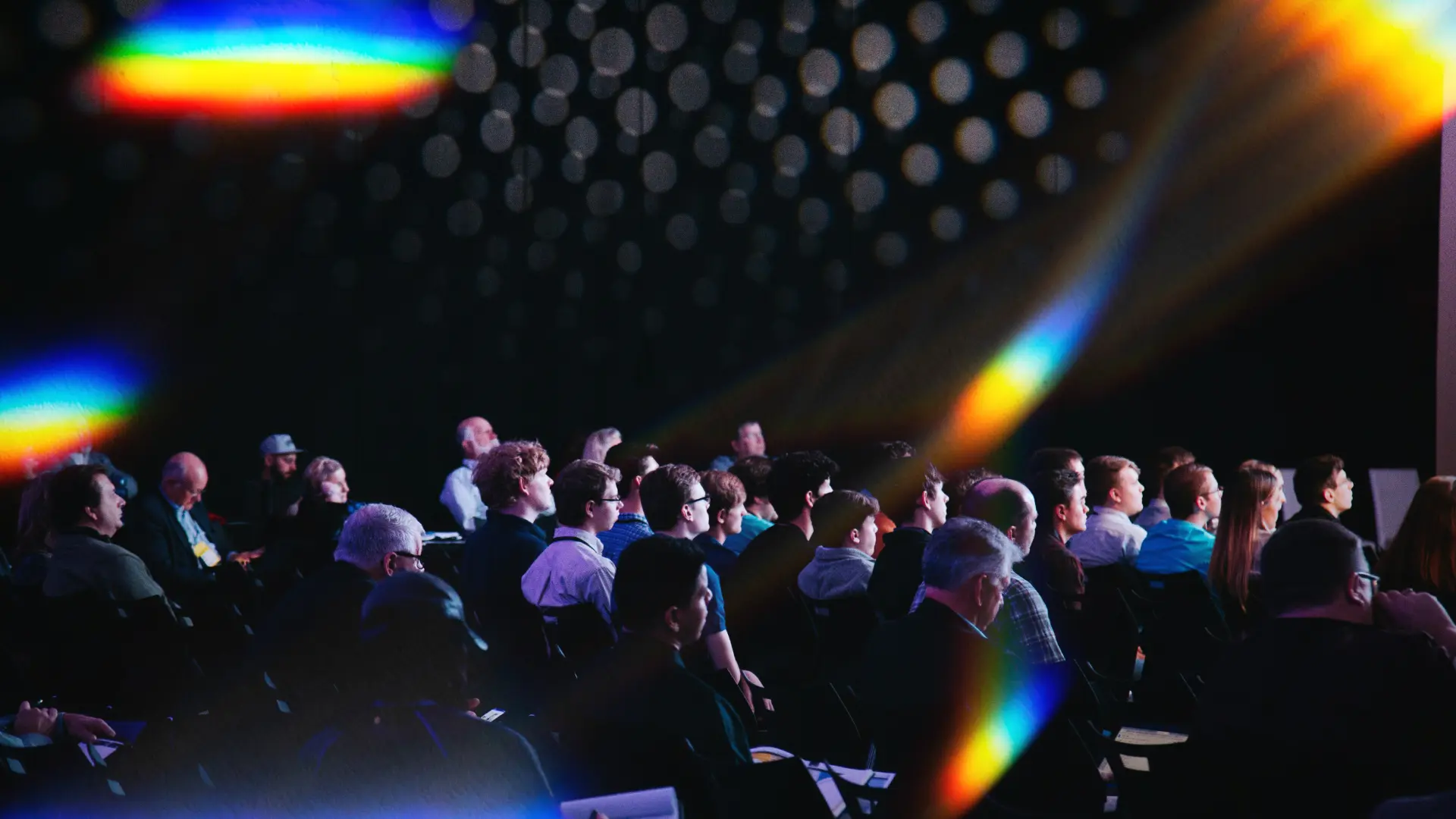 Audience seated at a business event or conference, showcasing attendees listening in a dark venue — photo by @headwayio from the image “Crowd of people sitting on chairs inside room” (source: Unsplash).